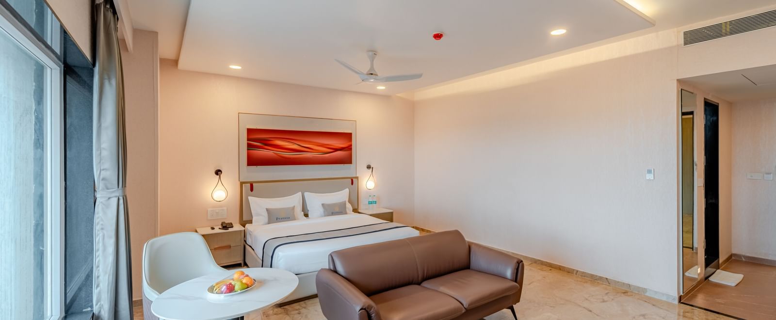  A spacious room with a king-size bed, a sofa, and a wall-mounted television | Studio Suite | Pravasa Hotel, Vijayapura