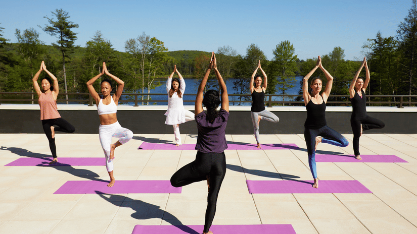 A group of women on a sunny day practising yoga on yoga mats with the view of the lake in the background at YO1 Longevity & Health Resorts