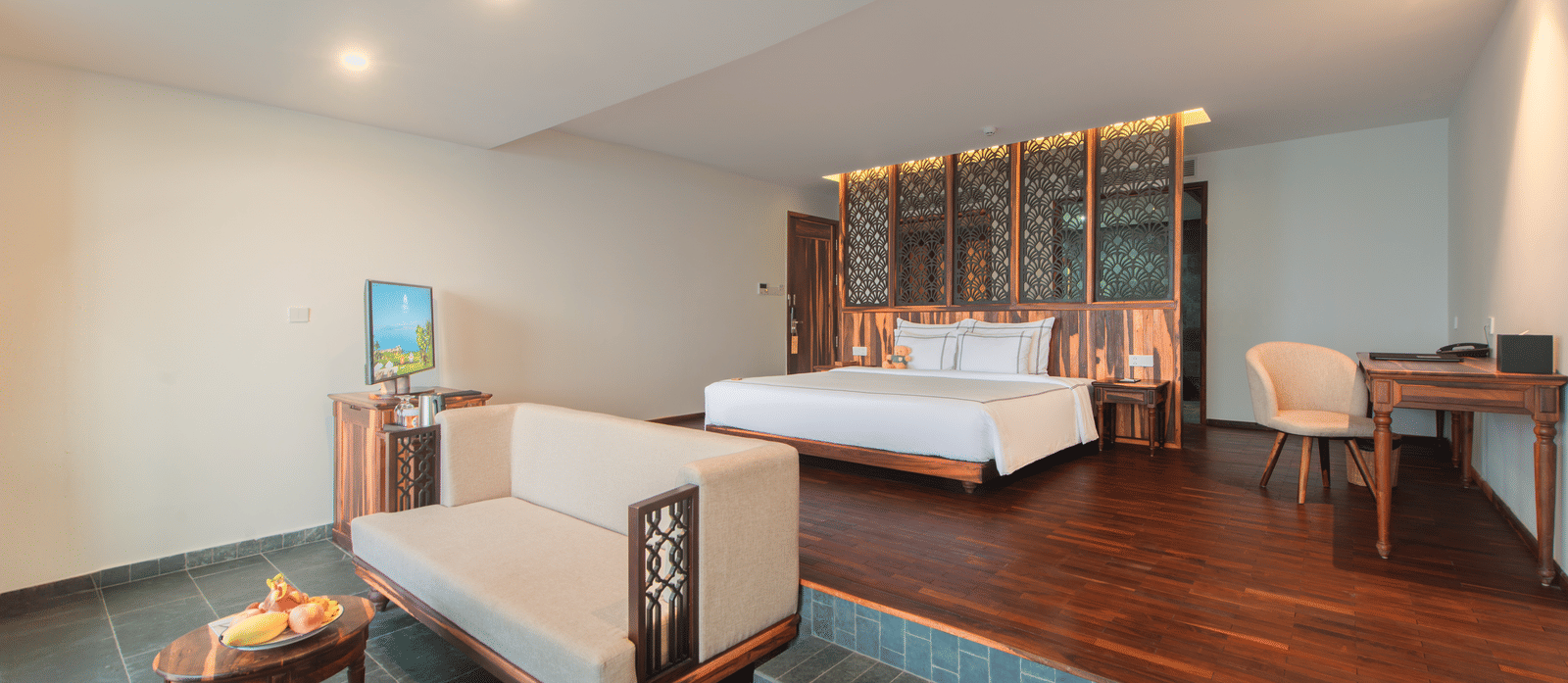 Suite interior at Alibu Resort Nha Trang, Vietnam, showcasing raised bed area, sofa bench, coffee table, television, wooden platform, and sliding doors for open living layout.