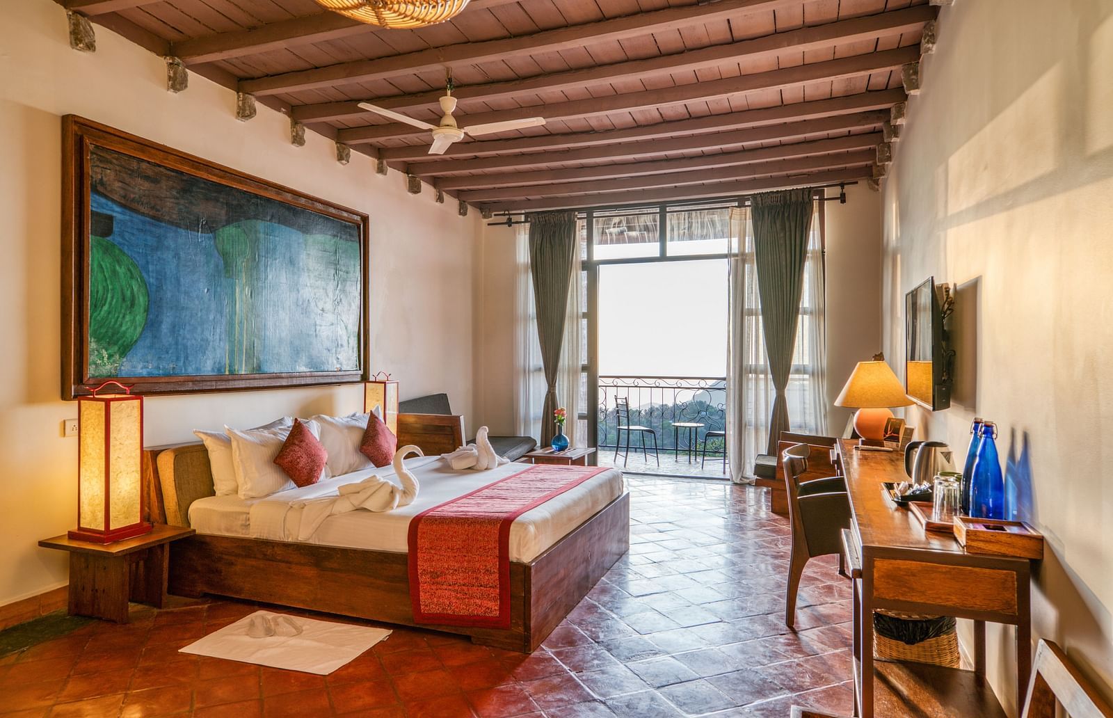 Large bedroom with a king-size bed, colorful artwork, and wooden furniture, leading to a balcony with a beautiful view of the landscape. | Mango Hill, Yercaud