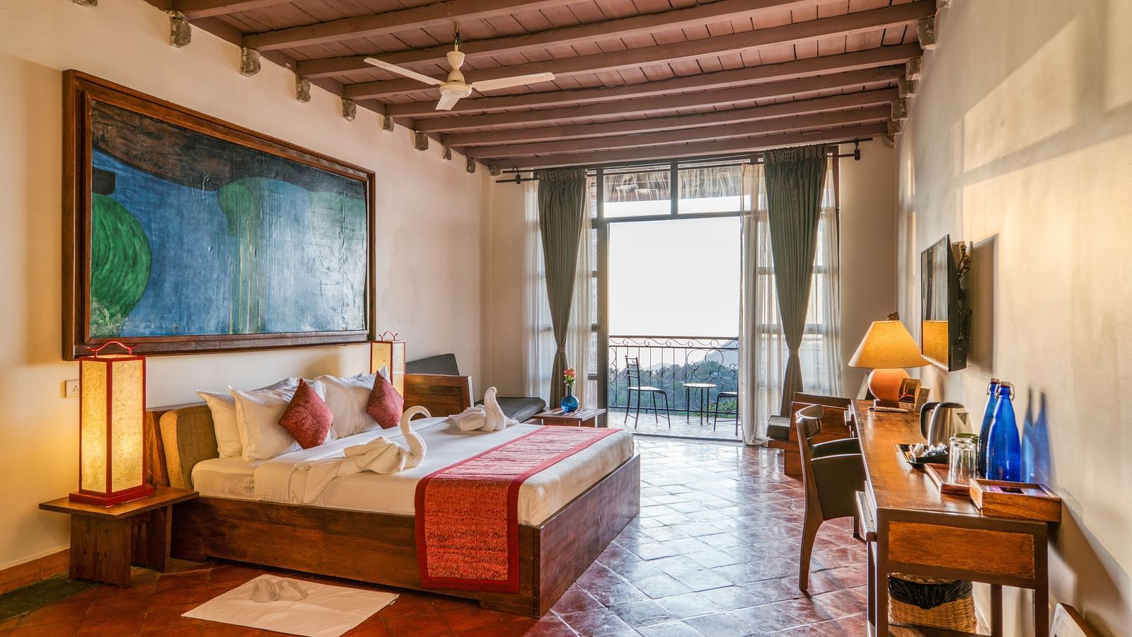 Large bedroom with a king-size bed, colorful artwork, and wooden furniture, leading to a balcony with a beautiful view of the landscape. | Mango Hill, Yercaud