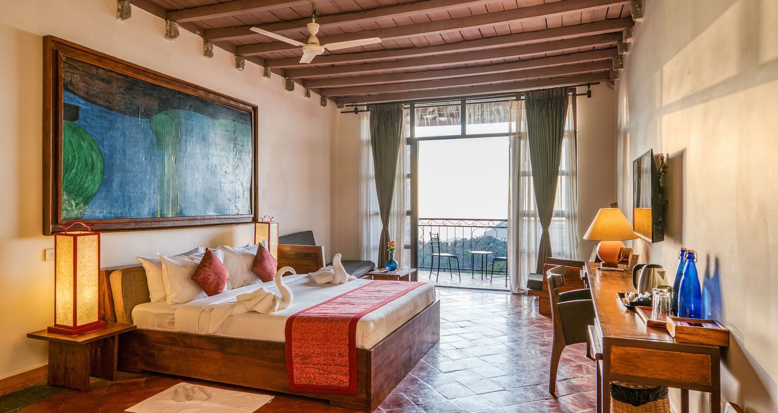 Large bedroom with a king-size bed, colorful artwork, and wooden furniture, leading to a balcony with a beautiful view of the landscape. | Mango Hill, Yercaud