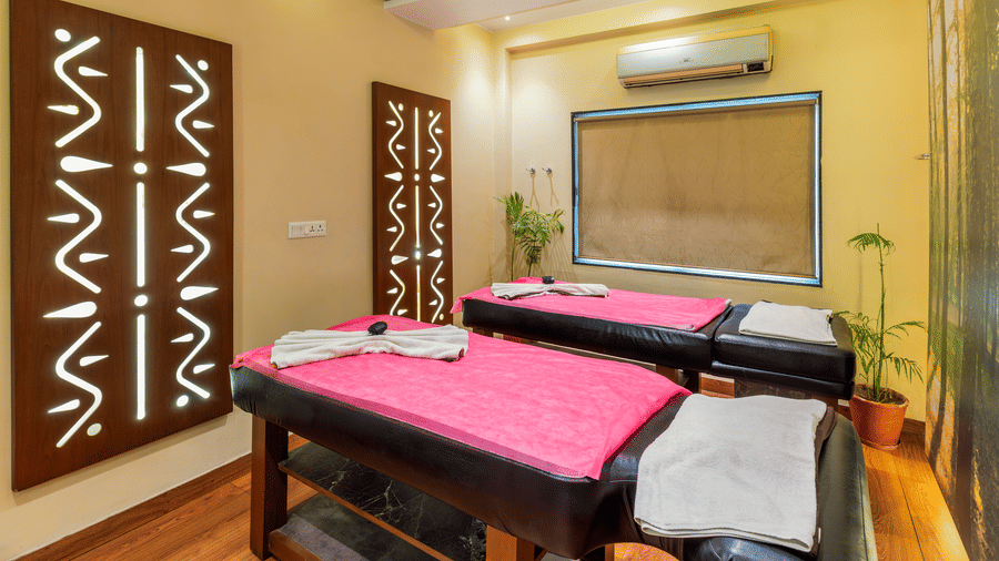 Interior of the Holistic Wellness Centre showing twin massage beds with pink linens and decorative wooden wall art - Amantra Comfort Hotel