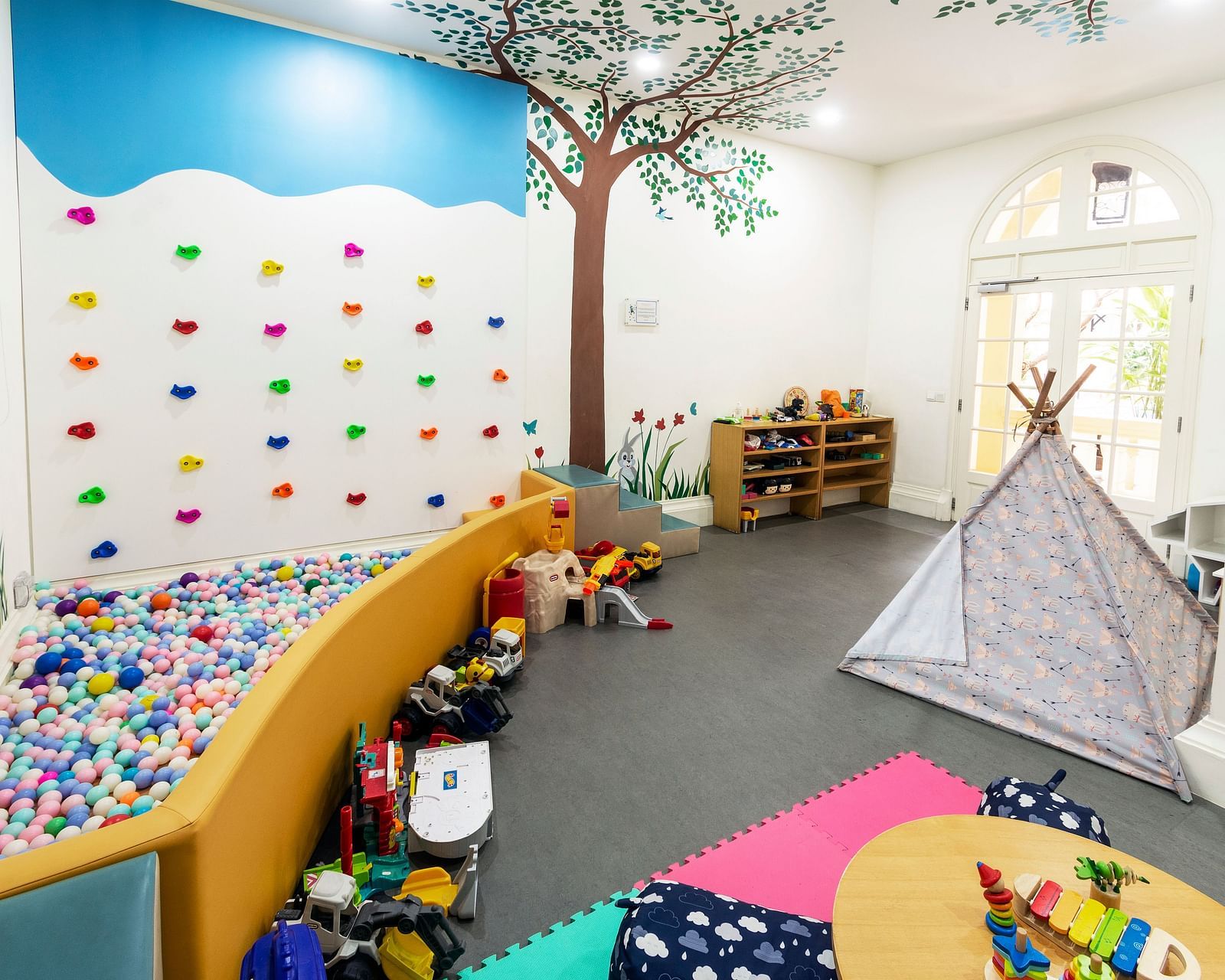 A colourful and playful children's playroom with a tree mural and various toys | Central Mansions, Phnom Penh