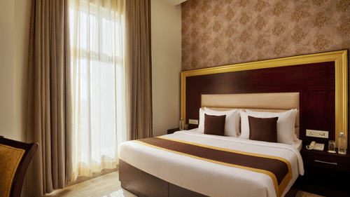 a double bed beside floor-to-ceiling windows in the STANDARD ROOM - Royal Kingdom Sarovar Portico, Pilibhit