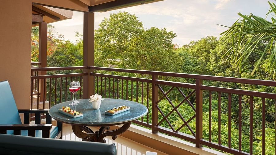 A table with beverages and snacks on a balcony overlooking lush green trees from Super Deluxe Room with Balcony at DGV Resort by Treat, Silvassa