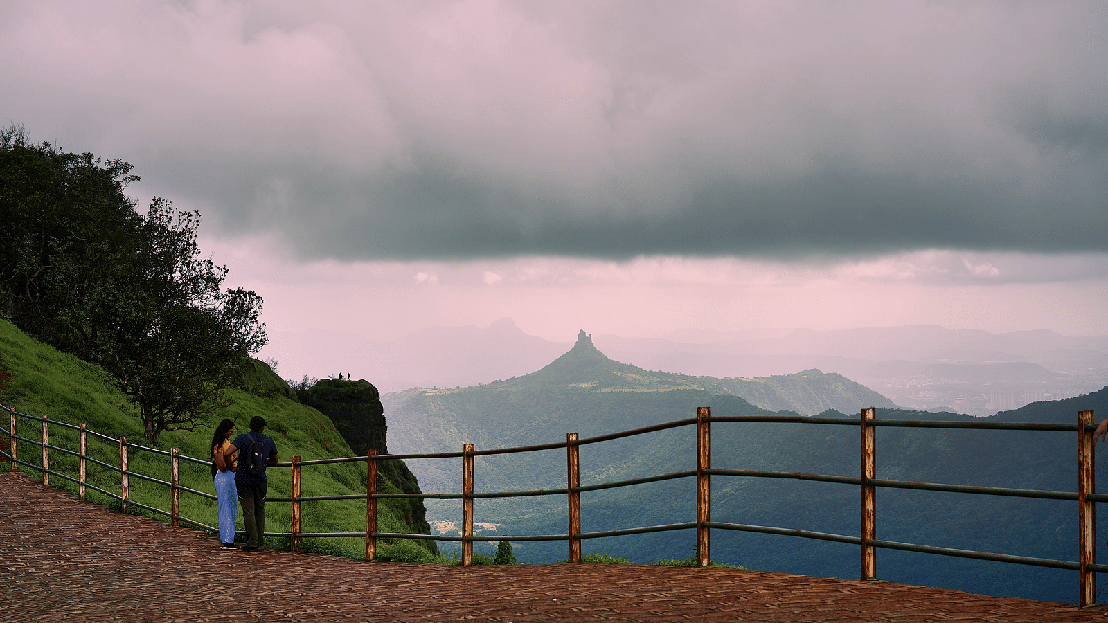 A couple standing next to a railing of the view point with mountains in the background