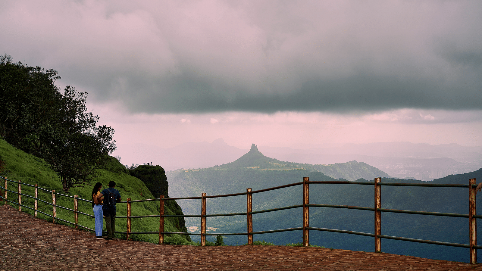 a couple standing at the end of a view point looking at the mountain 