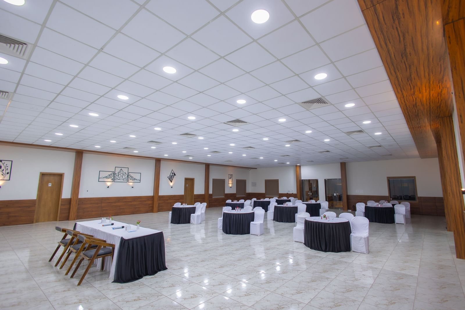The spacious banquet hall at the Daksh Eden Greenz with circular tables and chairs placed in a banquet style along with overhead lighting.
