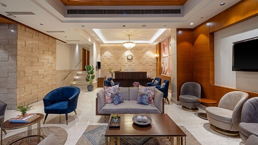 Lobby view with one center table and grey three seater sofa in the middle, and more chairs in the sides in pairs of two accopanied with coffee tables