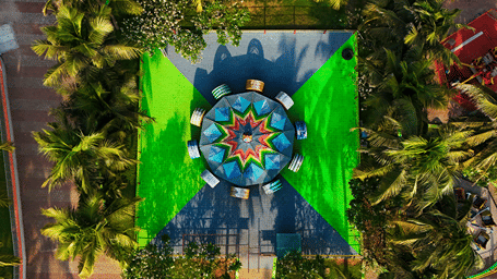 Overhead view of the Roll O Roll ride, a circular platform with a star-patterned centre on a green and grey square among palms at MGM Dizzee World, Chennai.
