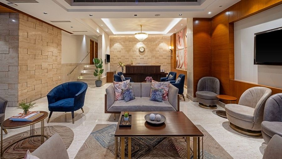 Lobby view with one center table and grey three seater sofa in the middle, and more chairs in the sides in pairs of two accopanied with coffee tables