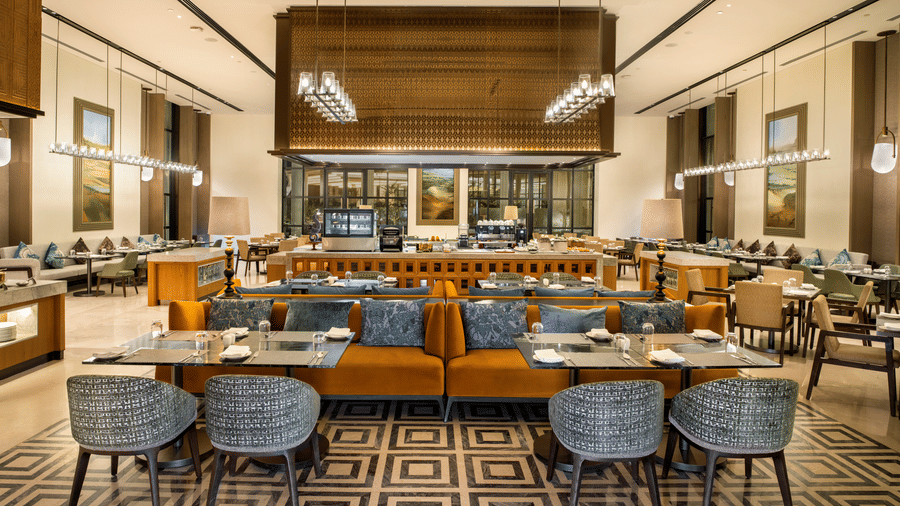 View of CHITHIRAI restaurant at The Residency Signature Madurai with dining tables, blue chairs, patterned flooring, and warm ambient lighting.