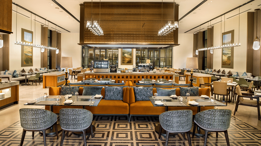 Dining area with blue banquette seating and wicker chairs at Chithirai restaurant, The Residency Signature Madurai, filled with natural light