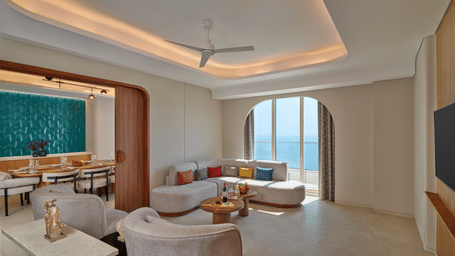 The Royal Ambassador suite living area at Swosti Premium Beach Resorts, Puri, featuring a sofa, armchairs, a small dining table, and a large window.
