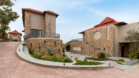 Beautiful stone resort villas with red tiled roofs sit along a paved pathway under a clear, bright blue sky - Sajjan Bagh Resort and Spa, Kumbhalgarh