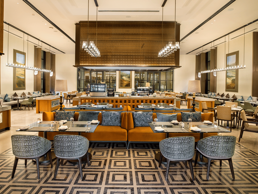 Dining area with blue banquette seating and wicker chairs at Chithirai restaurant, The Residency Signature Madurai, filled with natural light