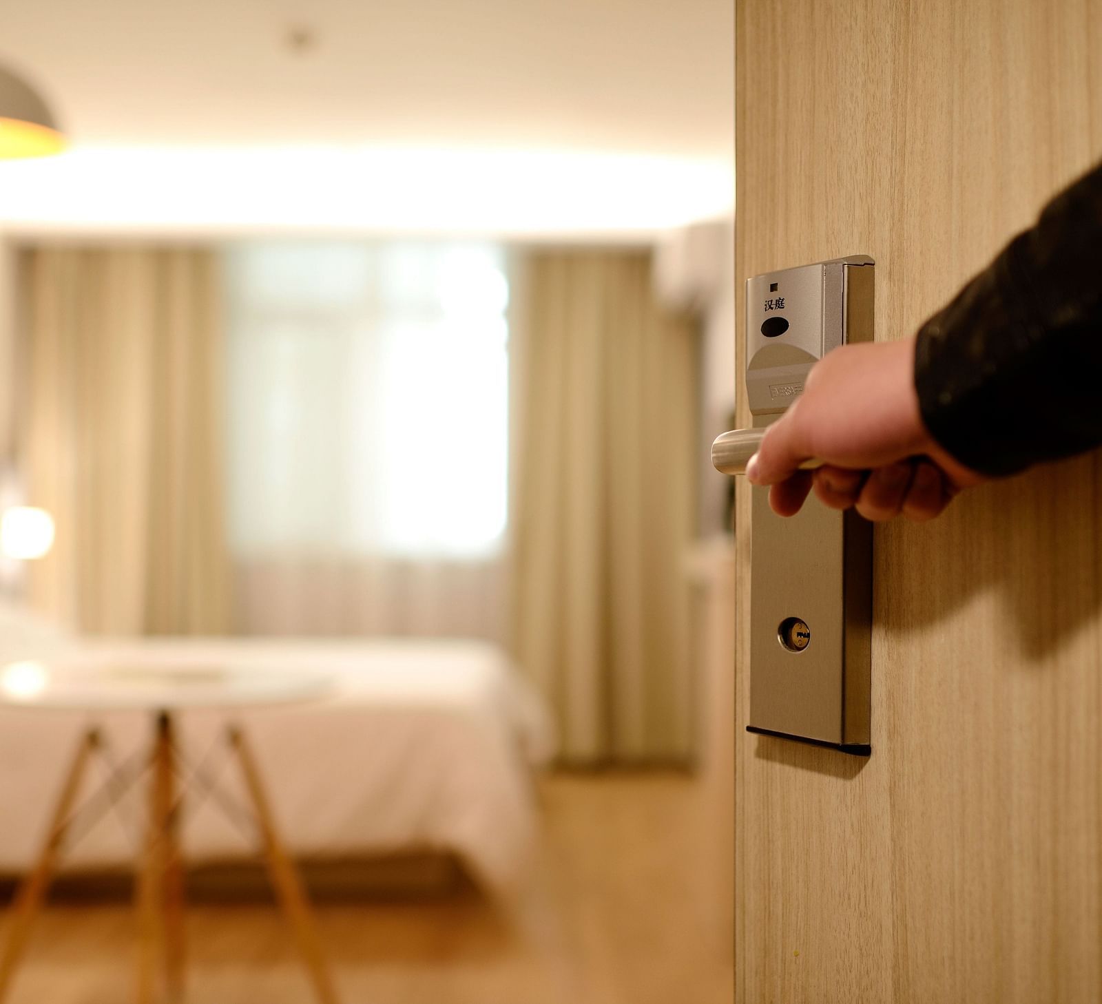 A hand opening a modern hotel room door, blurred background