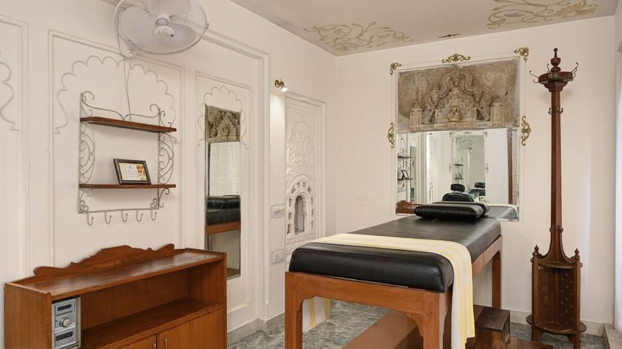 A spa room at Ram Pratap Palace, Udaipur featuring a wooden massage bed, ornate wall décor, mirrors, and vintage wooden furnishings.