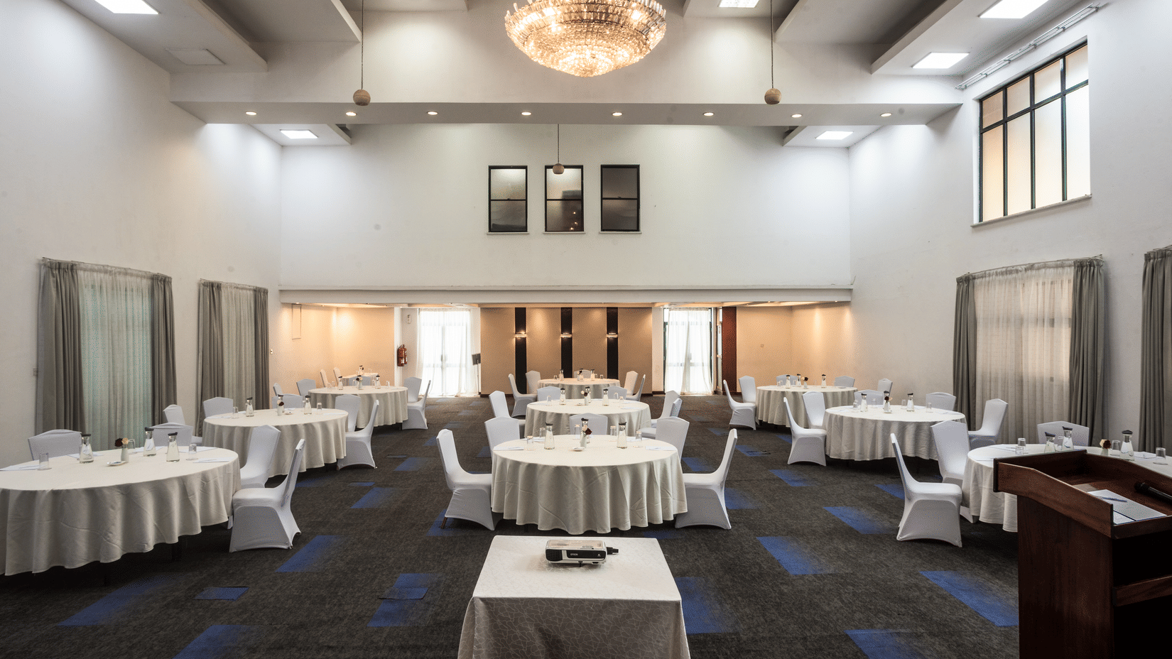 Spacious banquet hall with round table seating, elegant chandelier lighting, and large windows, set up for an event or conference.