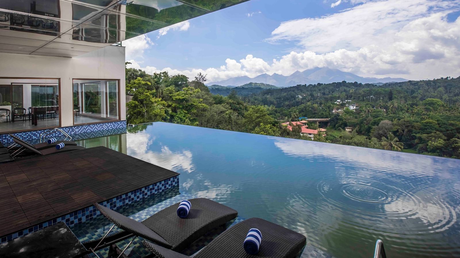 Image of the infinity swimming pool along with chairs and clear sky in the background | Great Trails Wayanad by  GRT hotels.
