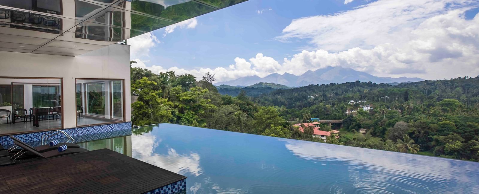Image of the infinity swimming pool along with chairs and clear sky in the background | Great Trails Wayanad by  GRT hotels.