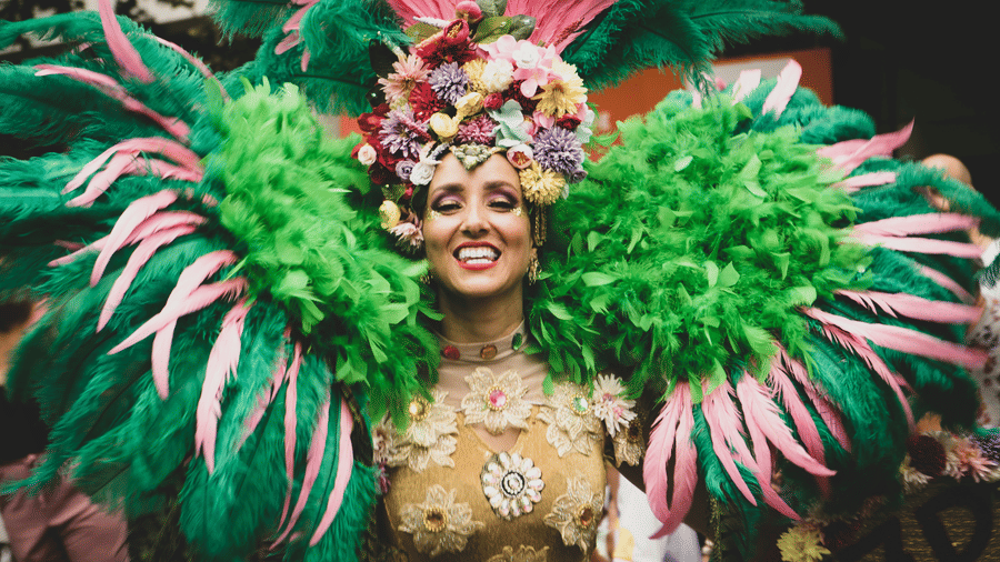 A woman wearing an elaborate green and pink feather costume and a colorful floral headpiece