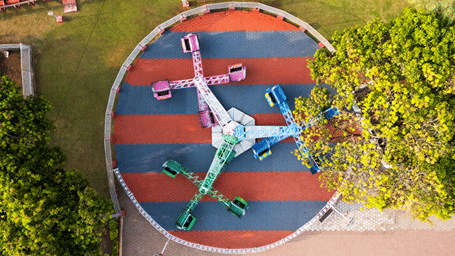 Overhead view of the Twister ride with four arms holding pink, blue and green cars over a red and blue striped circular base at MGM Dizzee World, Chennai.