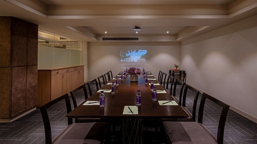 A meeting room at Saket 27 featuring premium wooden-framed dark brown chairs and a table, with a projector at one end.