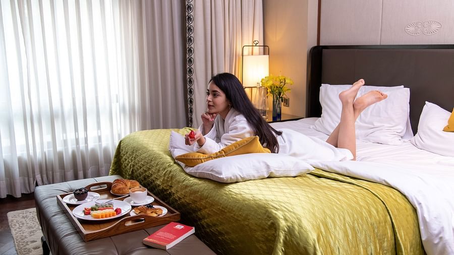 image of a woman relaxing on the bed with a platter of breakfast served - The Claridges New Delhi