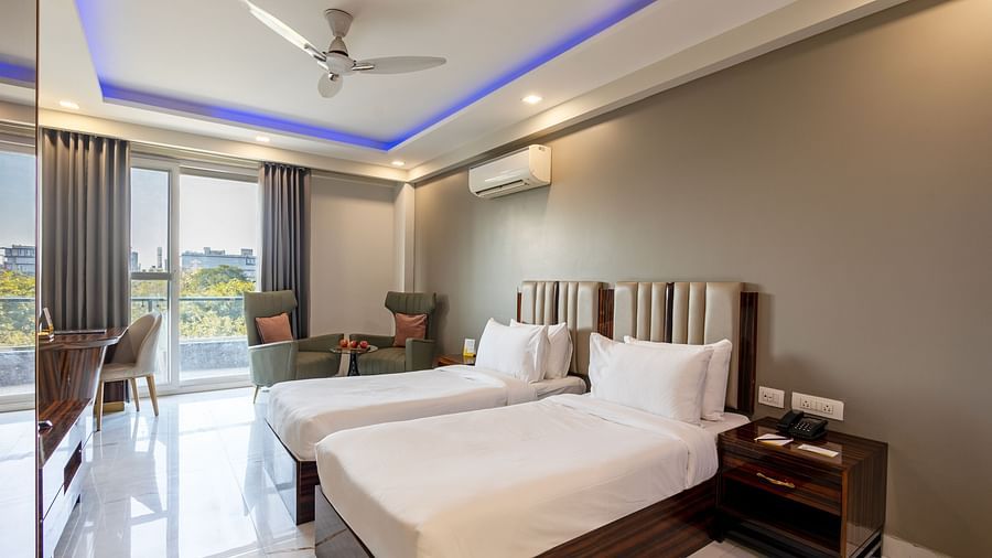 A room with twin beds, soft lighting, a ceiling fan, and a huge glass door at Hotel Bawa, Gurgaon.