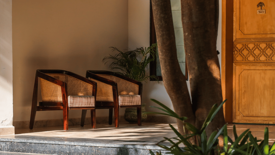 An outdoor area shows chairs with a small table placed on a stone surface beside plants and a doorway at Ananta Spa & Resort, Jaipur.