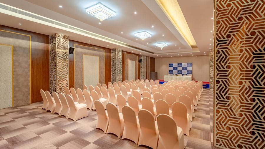Rows of neatly arranged chairs face a stage in a well-lit banquet hall | Meetings & Events | Pravasa Hotel, Vijayapura