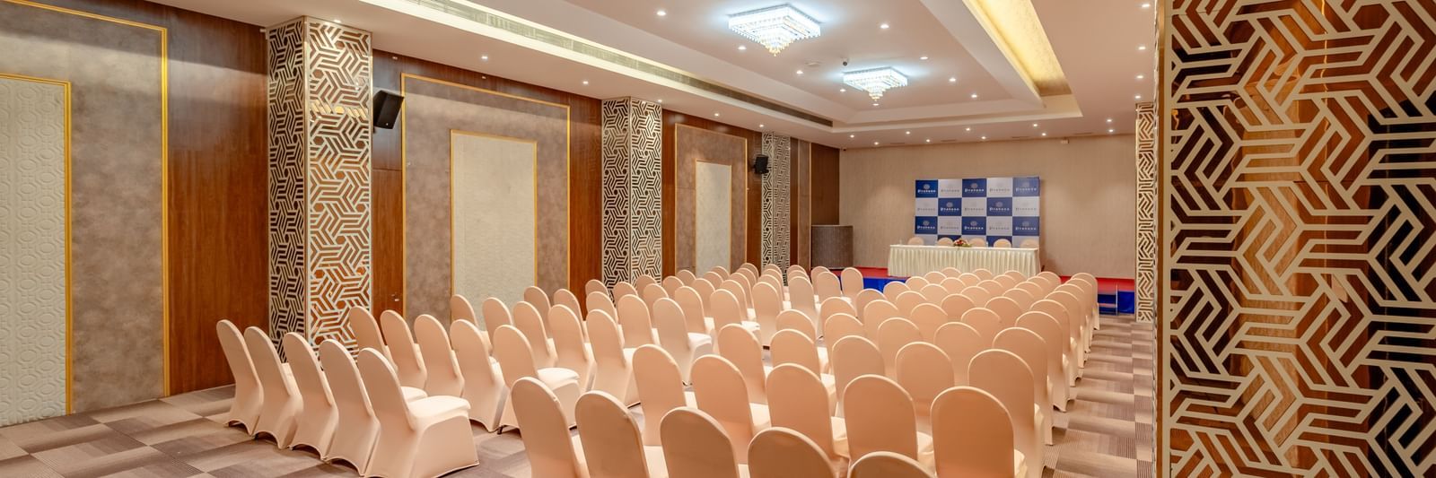Rows of neatly arranged chairs face a stage in a well-lit banquet hall | Meetings & Events | Pravasa Hotel, Vijayapura