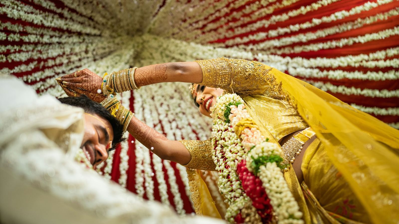 Bride lying gracefully under a decorative umbrella with traditional henna on her hands during an Indian wedding ritual.