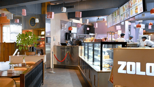 A bakery with a counter full of fresh baked goods, workers behind the counter