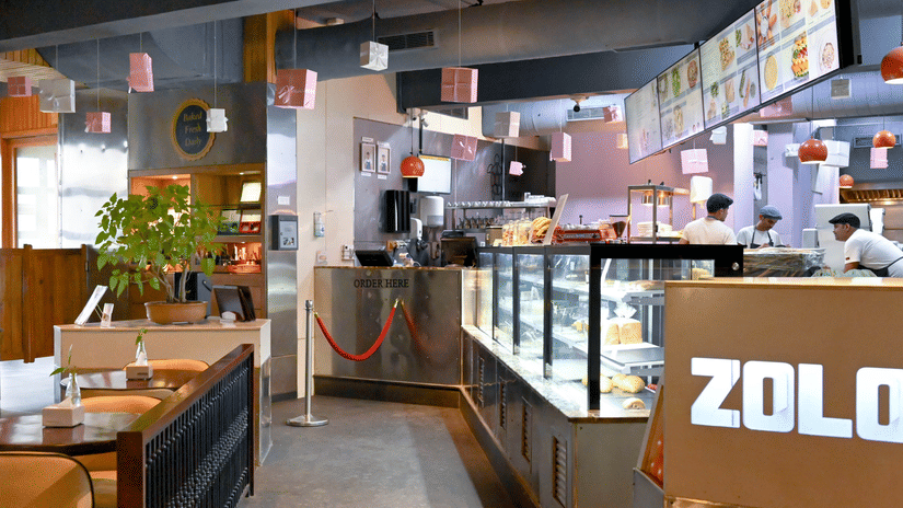 A bakery with a counter full of fresh baked goods, workers behind the counter