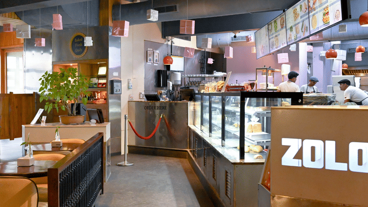 A bakery with a counter full of fresh baked goods, workers behind the counter