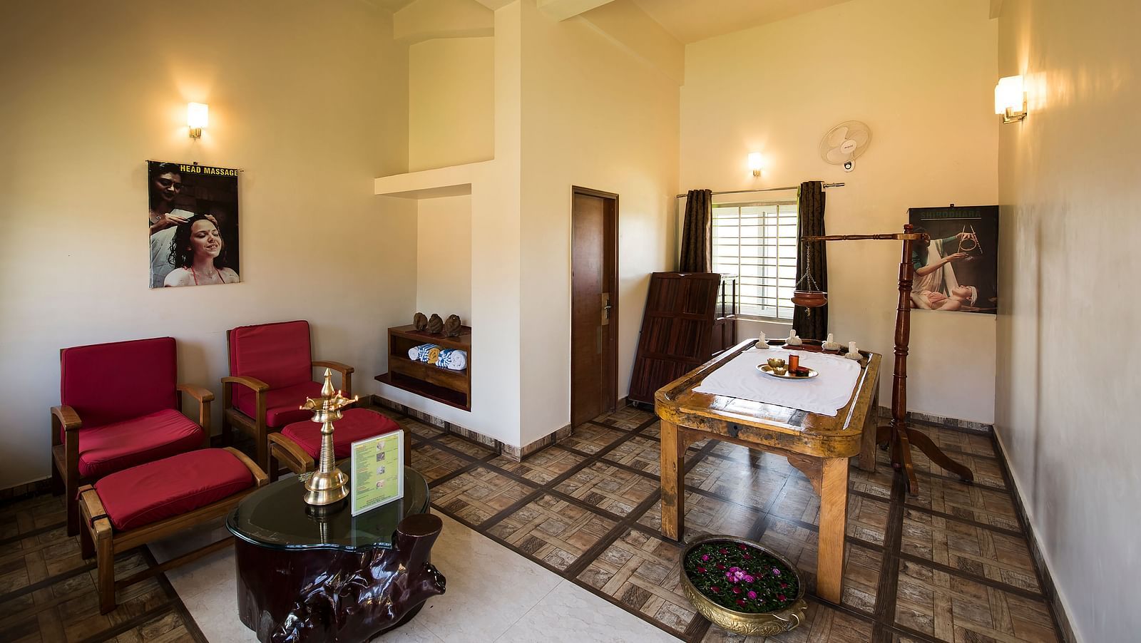 Ayurvedic Health Centre presents a waiting area with red chairs, a coffee table, and artwork on the walls | Woodstock Resorts, Coorg