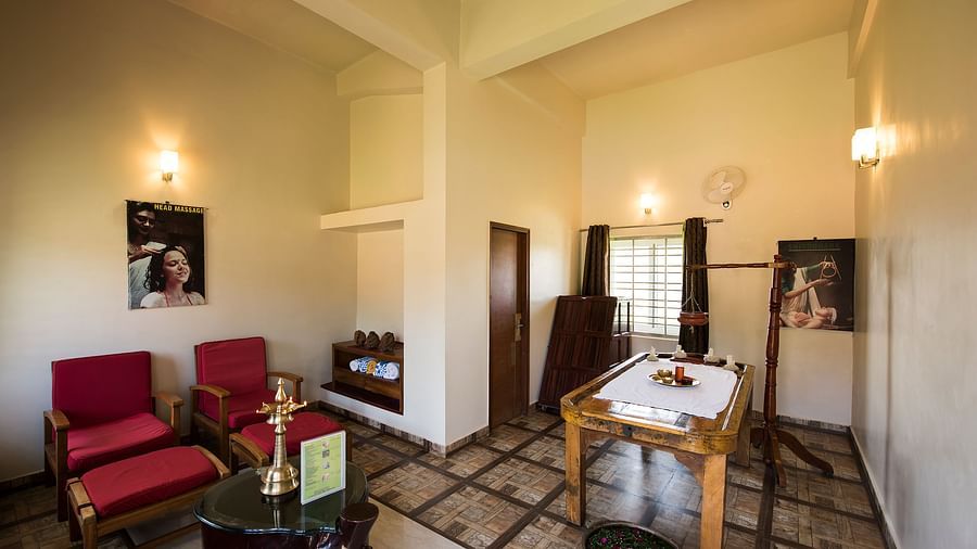 Ayurvedic Health Centre presents a waiting area with red chairs, a coffee table, and artwork on the walls | Woodstock Resorts, Coorg