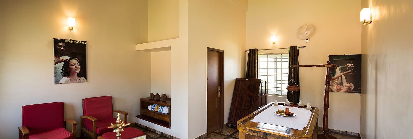 Ayurvedic Health Centre presents a waiting area with red chairs, a coffee table, and artwork on the walls | Woodstock Resorts, Coorg