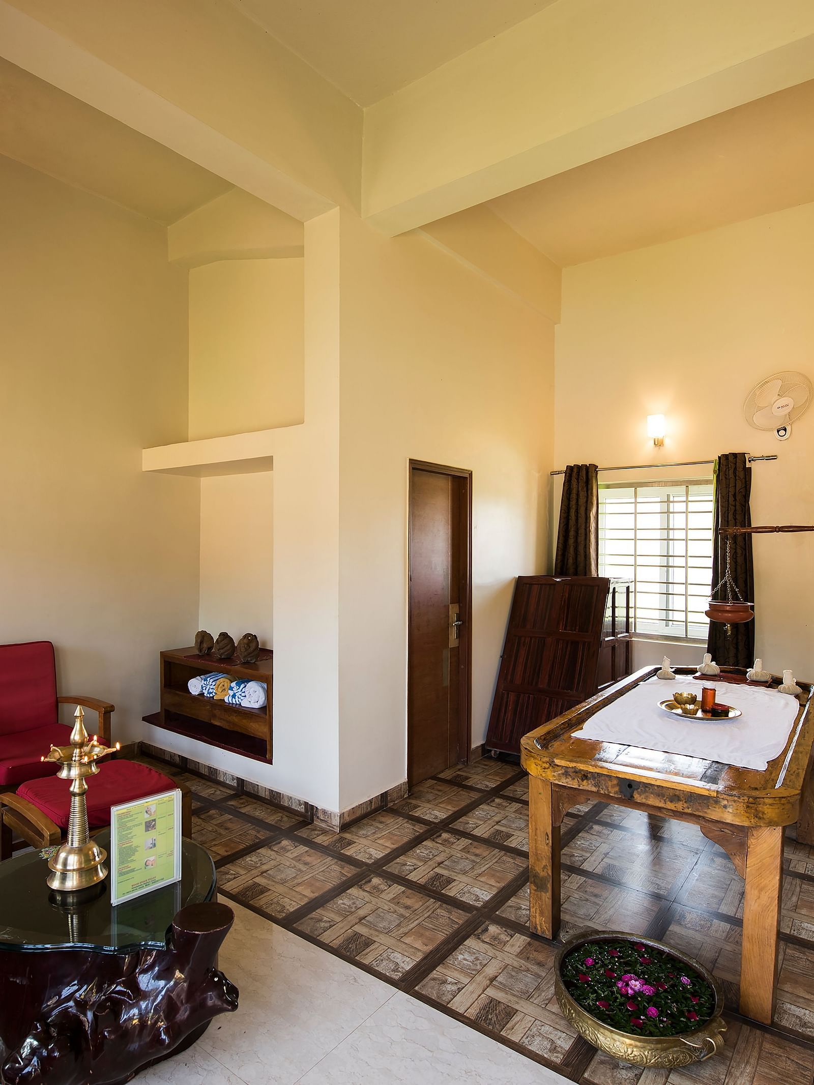Ayurvedic Health Centre presents a waiting area with red chairs, a coffee table, and artwork on the walls | Woodstock Resorts, Coorg