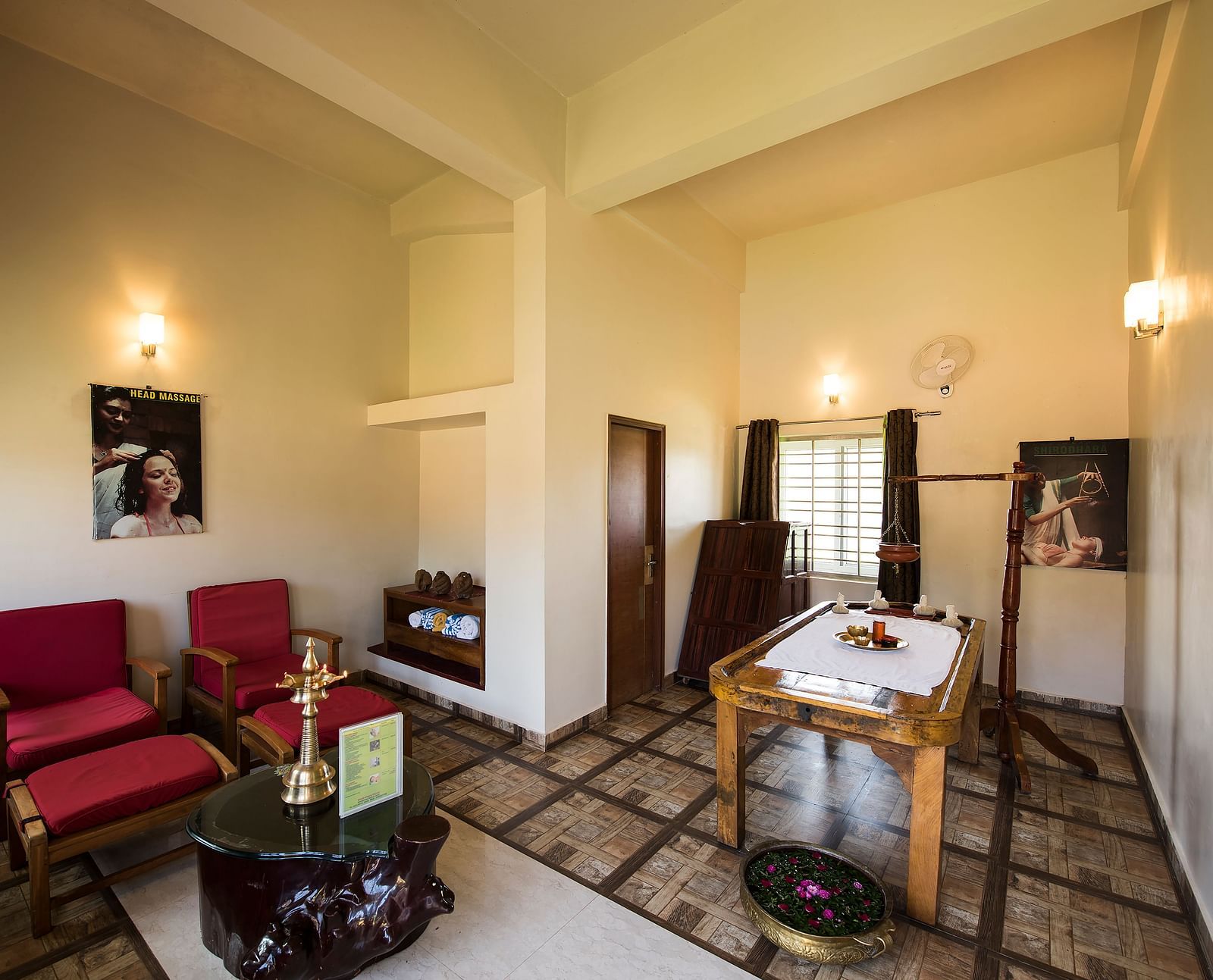 Ayurvedic Health Centre presents a waiting area with red chairs, a coffee table, and artwork on the walls | Woodstock Resorts, Coorg