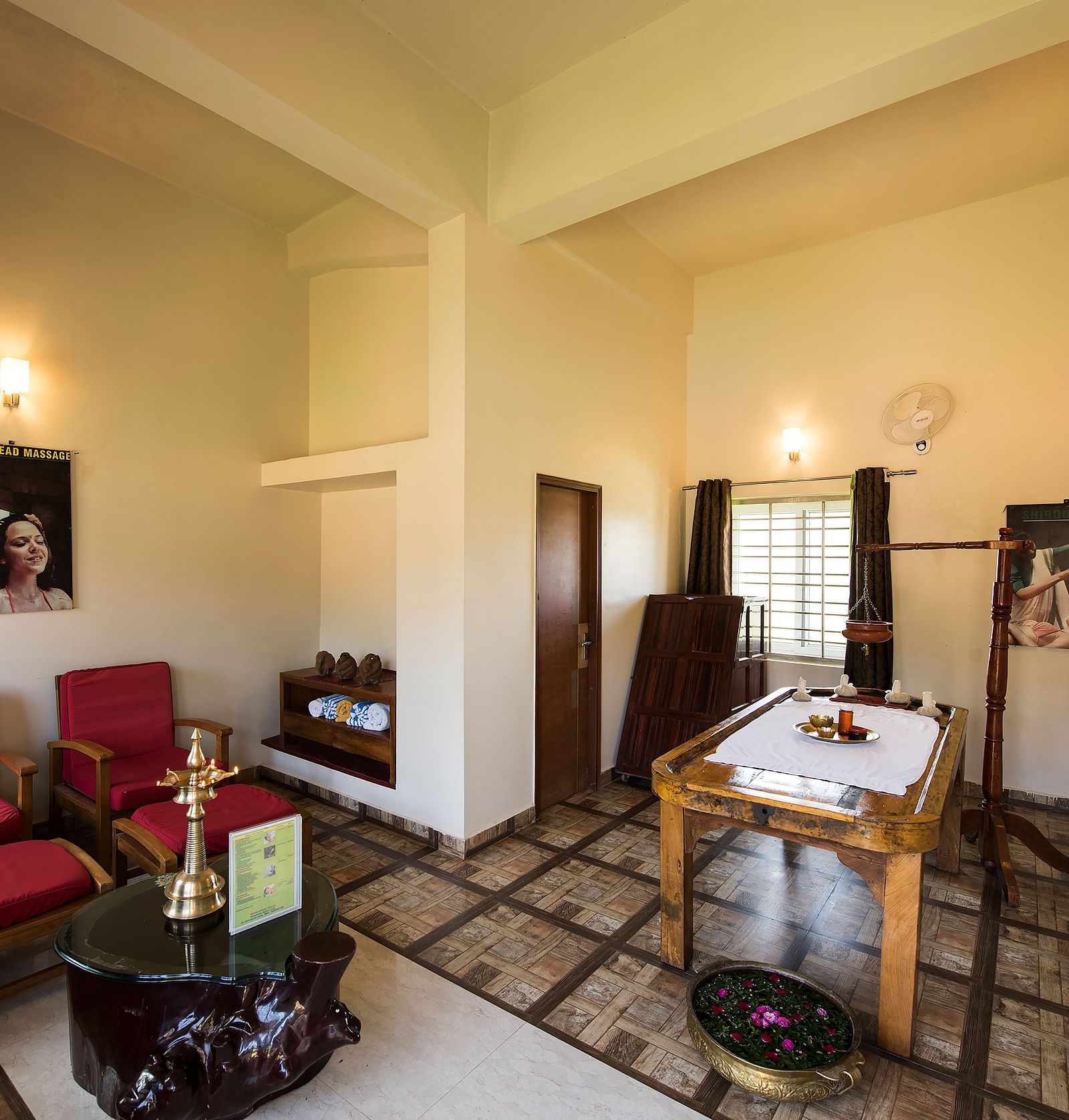 Ayurvedic Health Centre presents a waiting area with red chairs, a coffee table, and artwork on the walls | Woodstock Resorts, Coorg