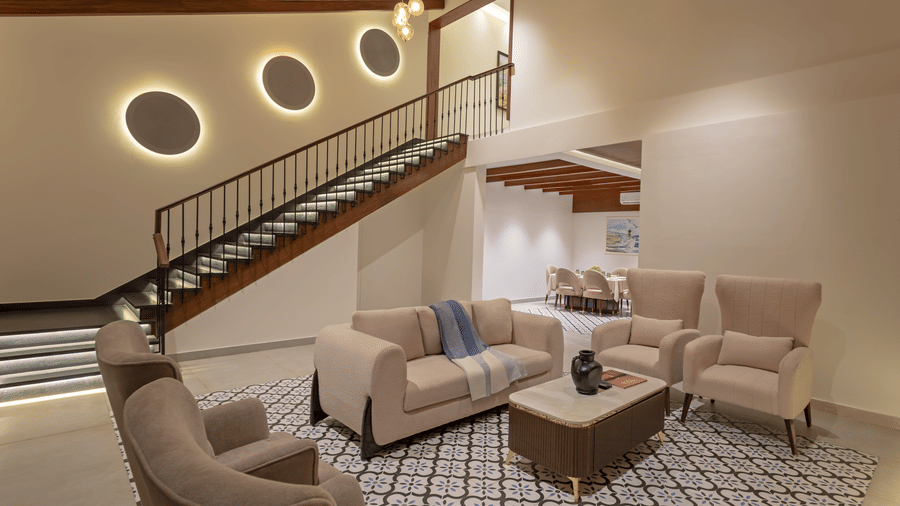 A modern living area with a sitting arrangement, a staircase, and circular wall lights illuminating the space - Lamrin Morjim Goa