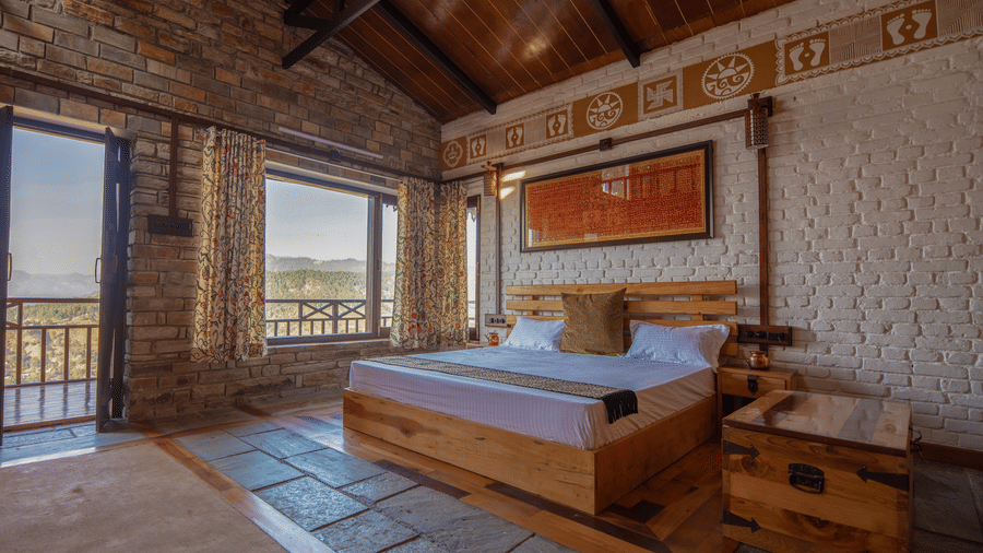 Room seating area with two wooden chairs, a rustic table, and a large window offering panoramic views of the lush mountains. - Blusalzz Homes The Himalayan Bungalow, Almora