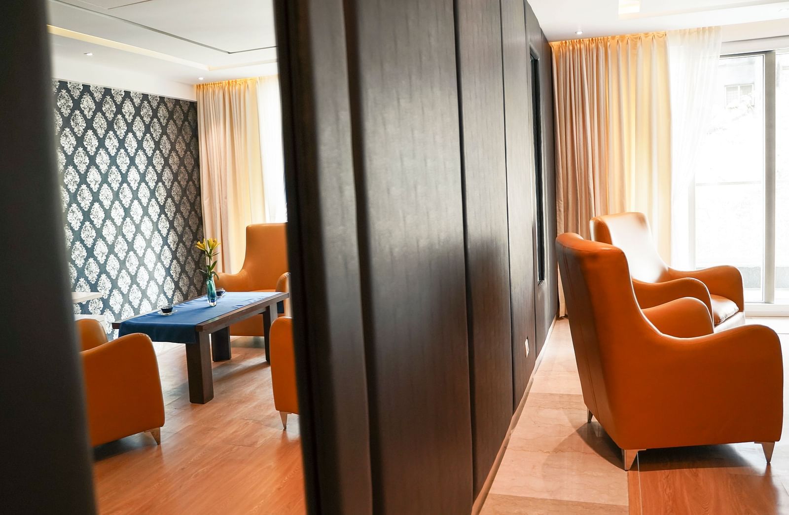 A sophisticated living area at BNGV Grandeur Hotel and Banquets, featuring dark wood accents, comfortable orange armchairs, and a small table.