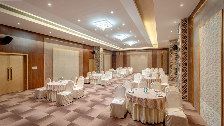 Conference room with round tables and beige chairs, ready for an event | Meetings & Events | Pravasa Hotel, Vijayapura