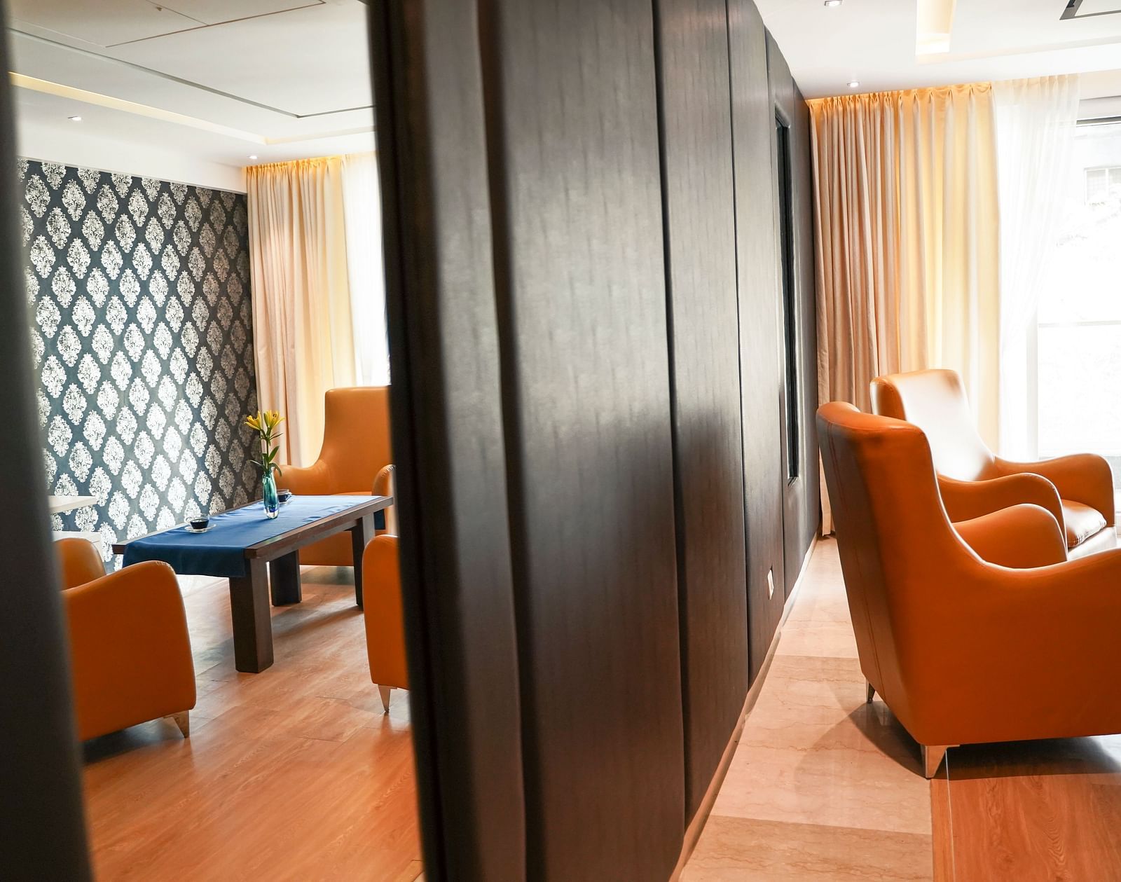 A sophisticated living area at BNGV Grandeur Hotel and Banquets, featuring dark wood accents, comfortable orange armchairs, and a small table.