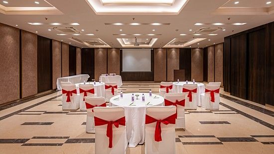 The conference space features a projector screen, with three round tables surrounded by chairs draped in white covers and accented with red ribbons on the back.